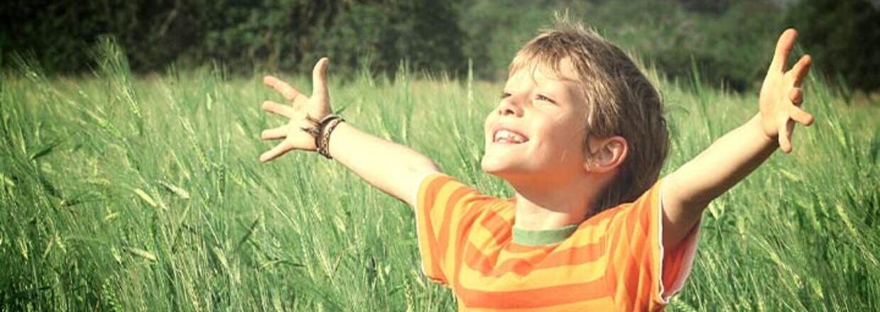 Bimbo in un prato verde che sorridendo guarda il cielo e spalanca le braccia
